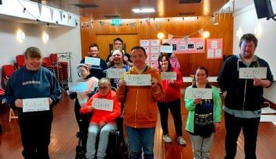 11 Members of the Encore Productions holding up signs of who their characters are.