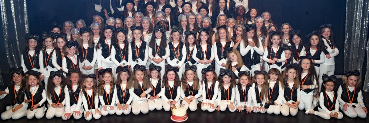 Group of children in matching sparkly, dance costume kneeling down and standing, posing for a group photo