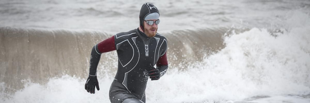 Swimmer Alan Corcoran in a wetsuit, running in ocean waves.