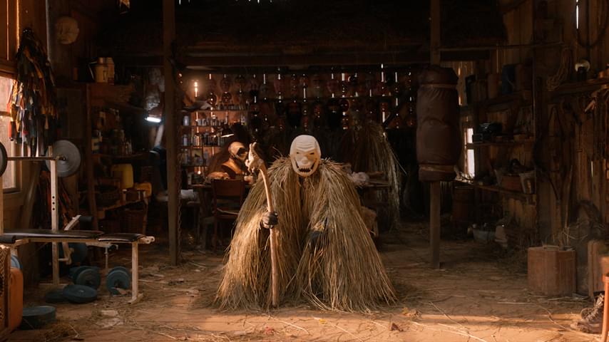 Man dressed in straw staring at the camera in a shed.