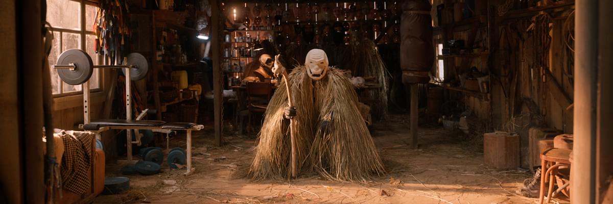 Man dressed in straw staring at the camera in a shed.