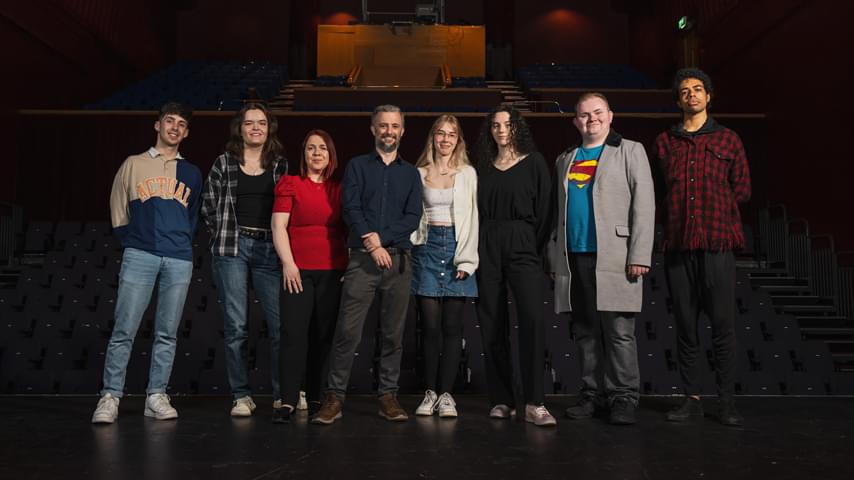 8 people stand on a stage with seats in the background