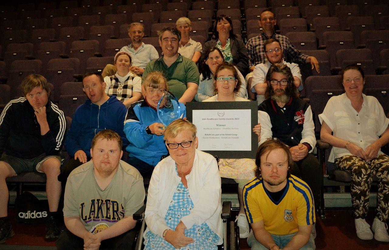 15 men and women with additional needs sit in theatre seats holding their award.