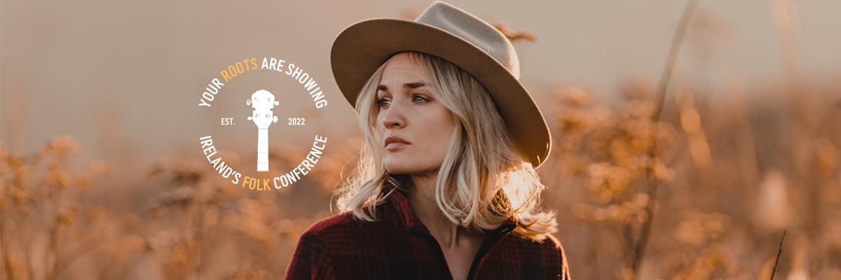 A blonde women looks to the left, standing in a wheat field. She wears a large beige hat and red sweater. 'Your Roots Are Showing | Ireland's Folk Conference' logo is to her left.