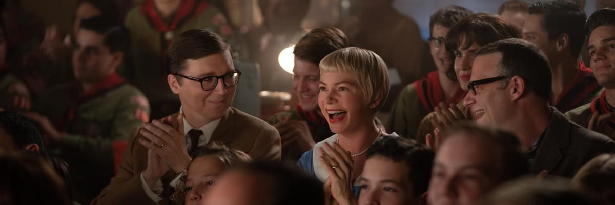 An 50s/60s style audience sit in a crowded theatre. An old fashioned project runs behind them. A young lady with a short blonde bob smiles widely at the screen in front of her. Her two gentleman friends look to her in amusement.