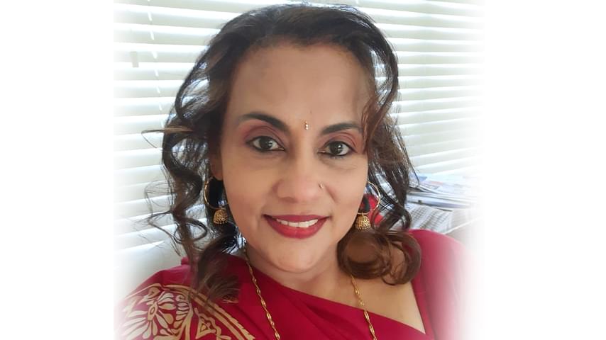 Writer in Residence and Author Radhika Iyer. Radhika has long, dark, curly hair, framing her face and a red bindi on her forehead. She wears a red and gold sari.