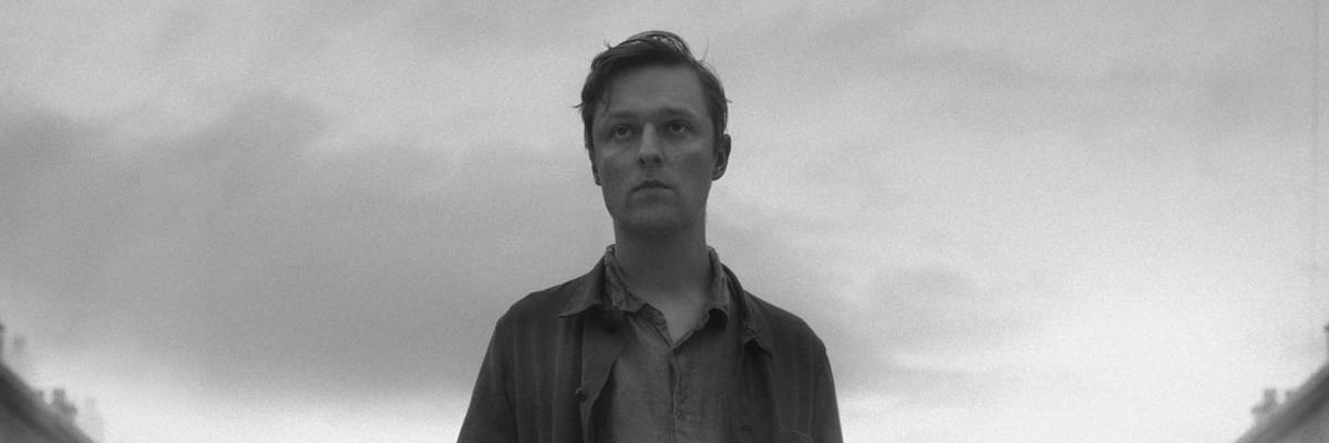 Black and white photo. A young men with a dark sky behind him.