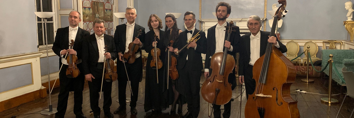 Eight people dressed in tuxes and black dresses holding violins, a trumpet and cello.