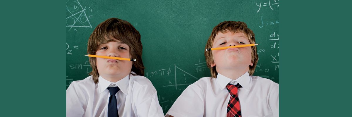 Two school boys hold pens in their mouth and wearing a white shirt and red ties