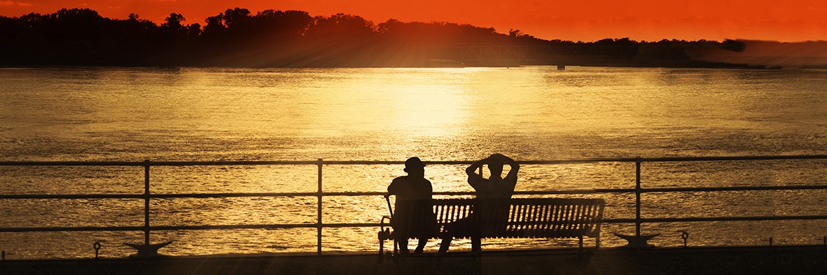 Two men relaxing on a park bench enjoying the riverside sunset