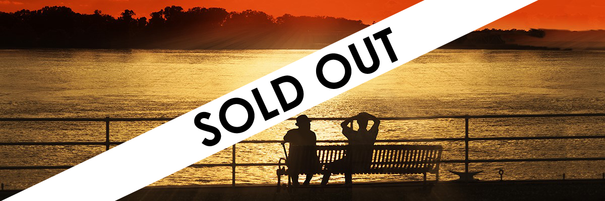 Two men relaxing on a park bench enjoying the riverside sunset. A white and black SOLD OUT sign is across the image