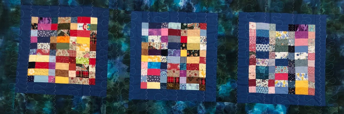 A dark blue quilt with three colour patchwork squares across it.