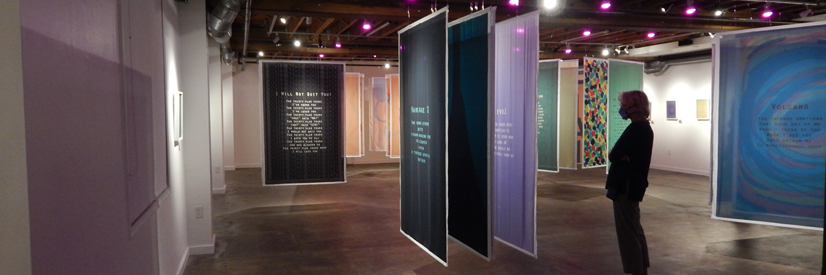 In a large room, large rectangles of coloured cloth hang from the ceiling, with poetry written on them.
