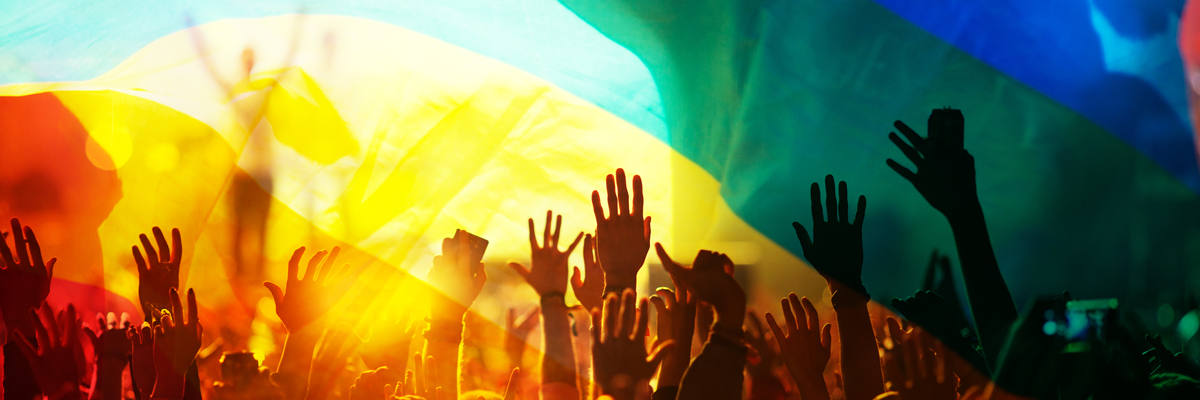 Silhouette of a parade of people with a rainbow flag flying above them