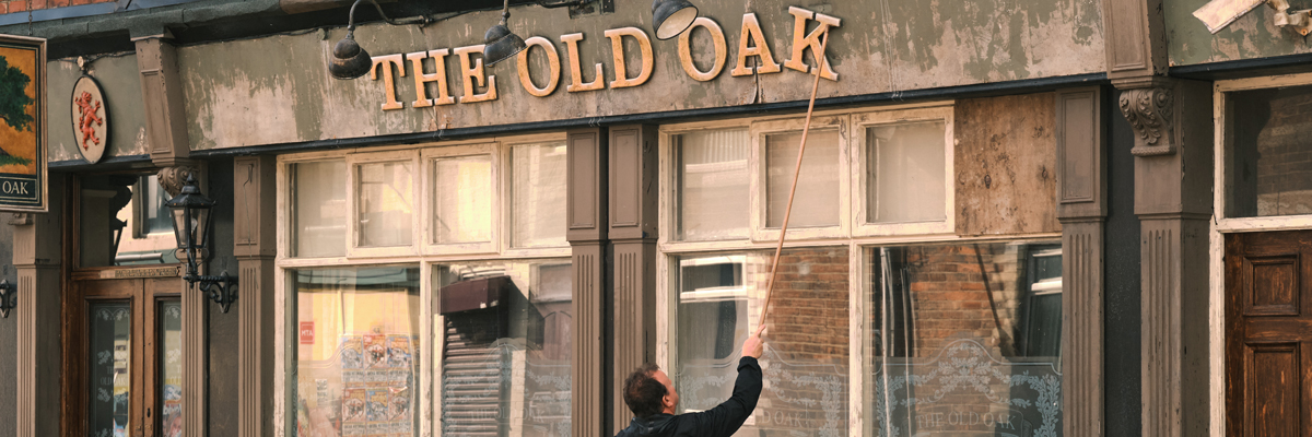 A man tries to fix a letter on the sign of a run down old pub building